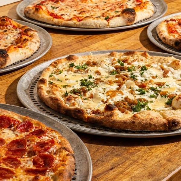 Five pizzas with various toppings, including pepperoni, cheese, and white sauce, on a wooden table.